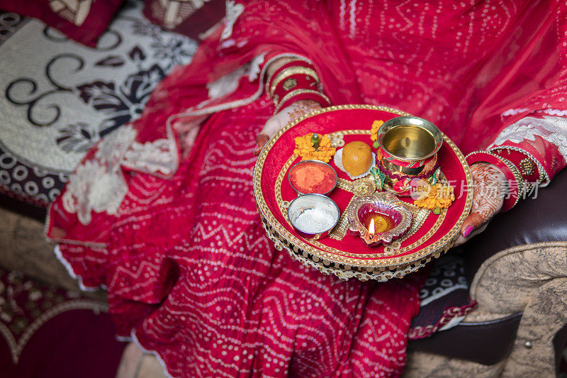 传统的印度妇女在Karwa Chauth节上拿着一个装饰着油灯、甜食、鲜花和宗教祭品的盘子。